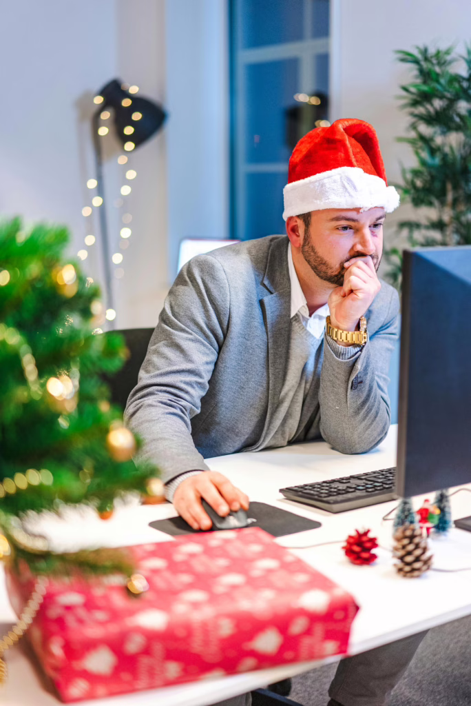 Adult man in Santa hat working at a decorated office desk during Christmas.