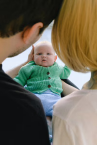 A family warmly gazing at their smiling baby indoors, symbolizing love and togetherness.